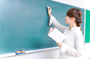 教科書を見ながら黒板に文字を書こうとする女性教師